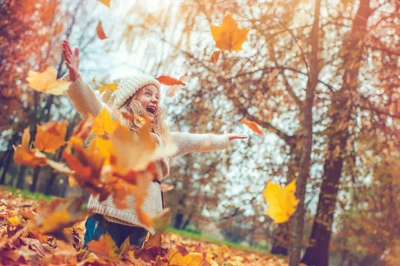 Little girl playing with the leaves in the foliage