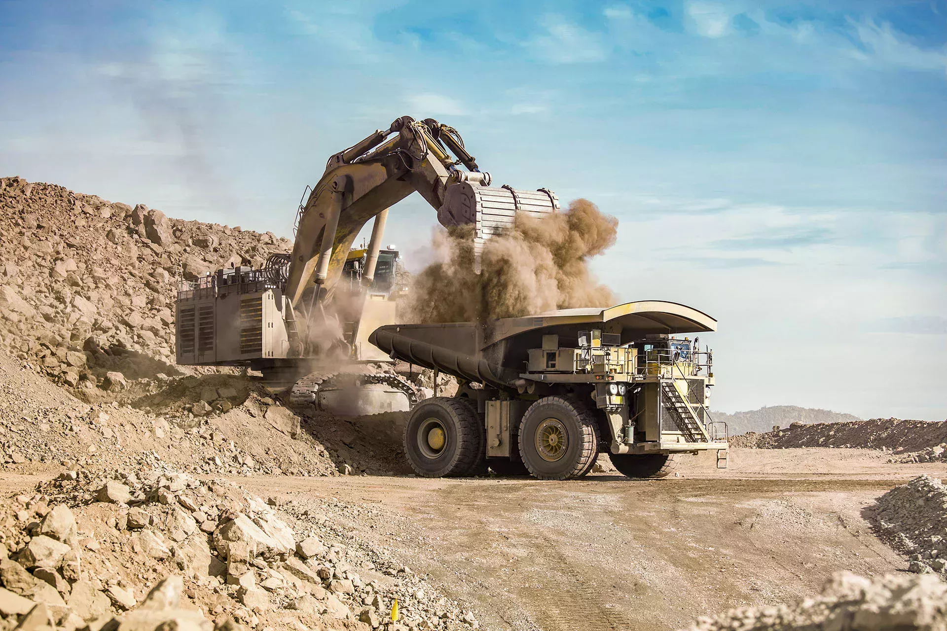 Excavator unloads bucket of dusty soil into large dump truck