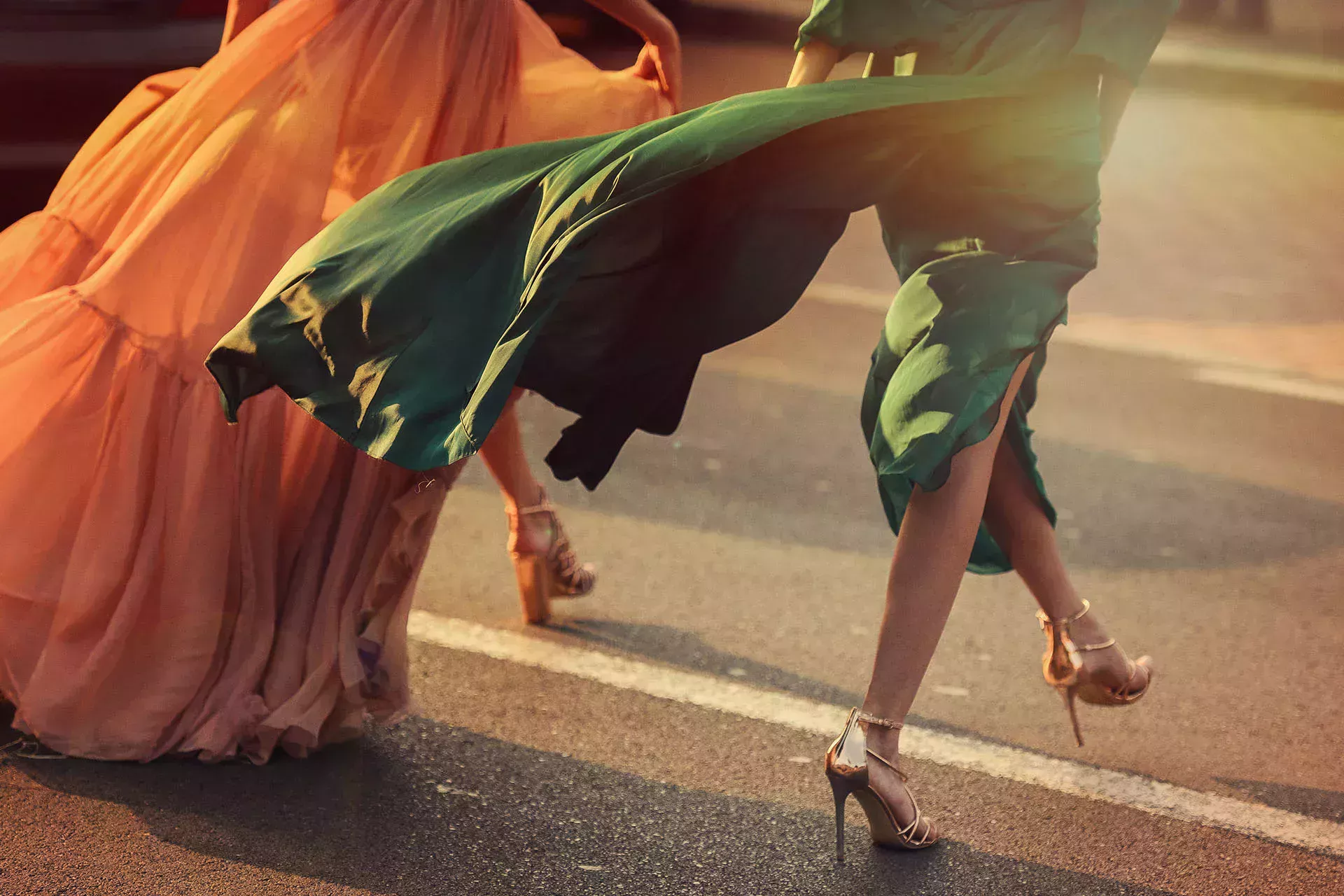 People in long dresses cross the street in high heels